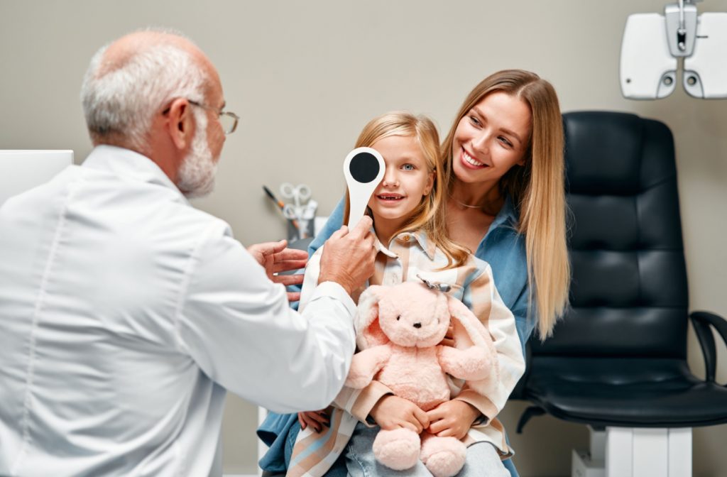 A parent holds their child, who holds a pink stuffed rabbit, as emotional support during an eye exam