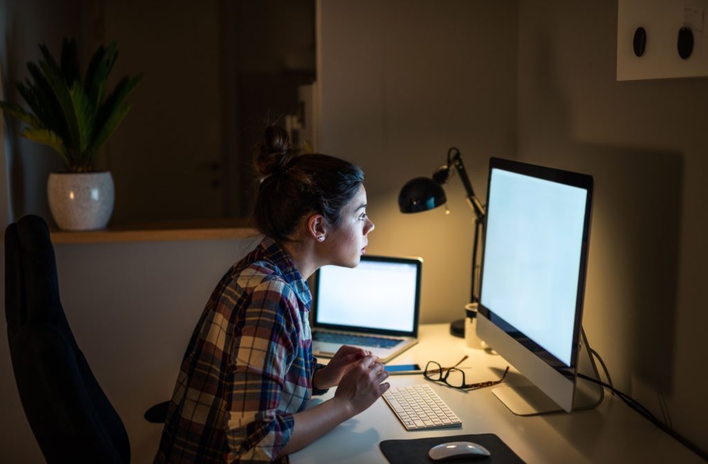 A woman staring at a computer screen in a dark office, feeling the effects of digital eye strain