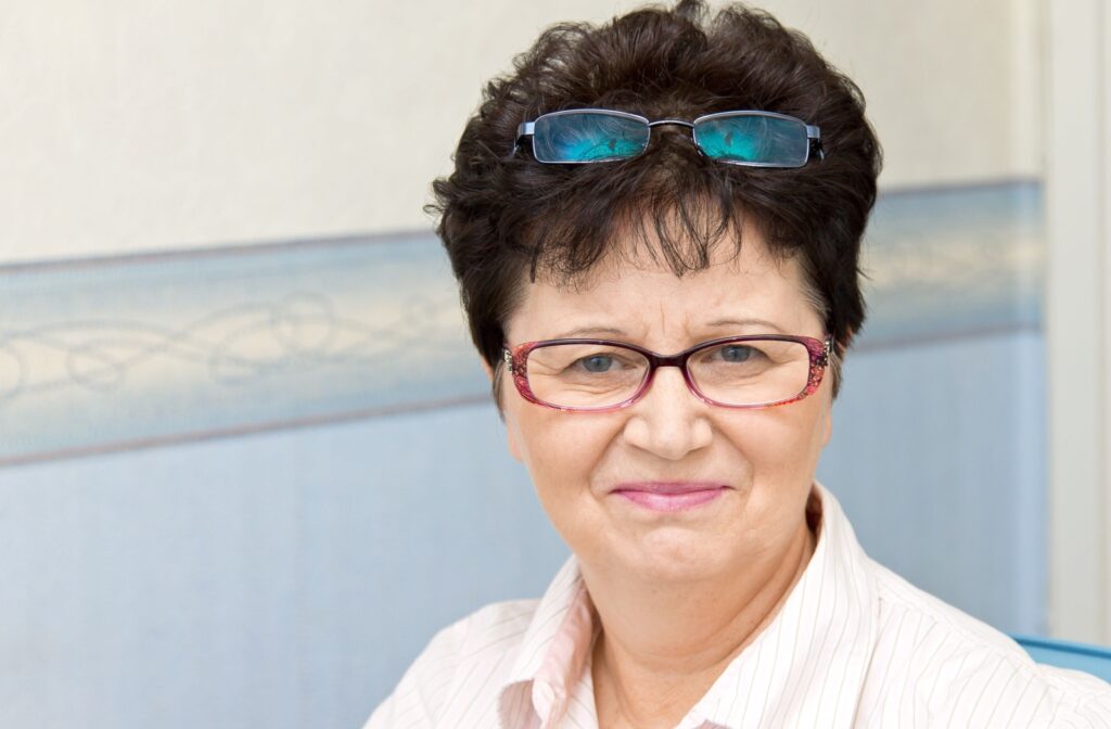 A senior person wearing two pairs of eyeglasses; one on their head and one on their face.