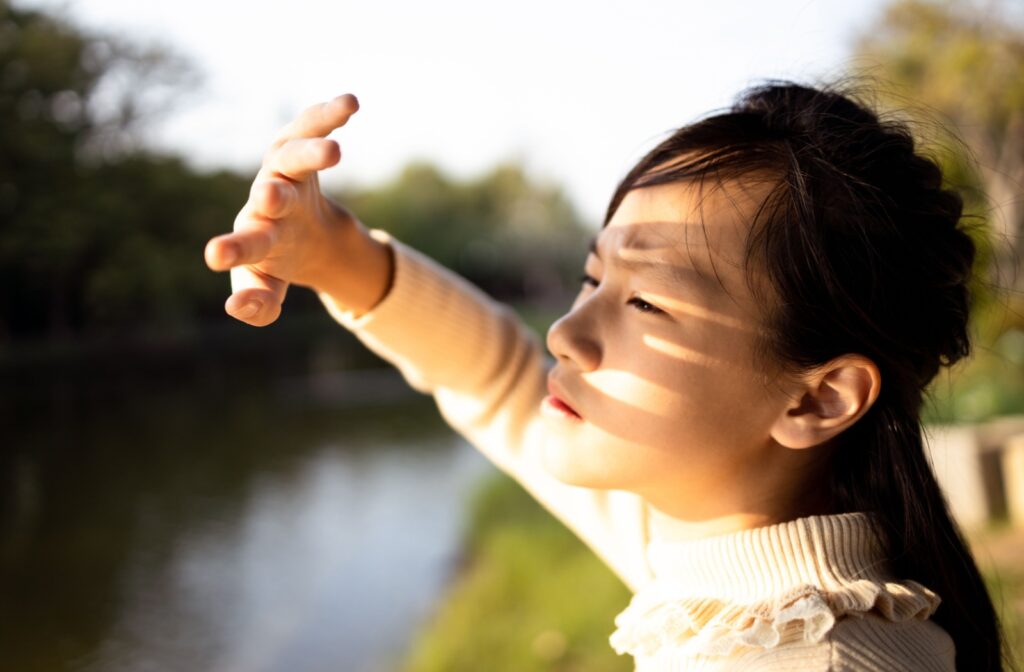 A person squints and shields their eyes from intense sunlight.