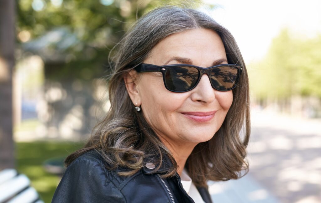 A stylish middle-aged adult wears a pair of high-quality, black sunglasses while smiling.
