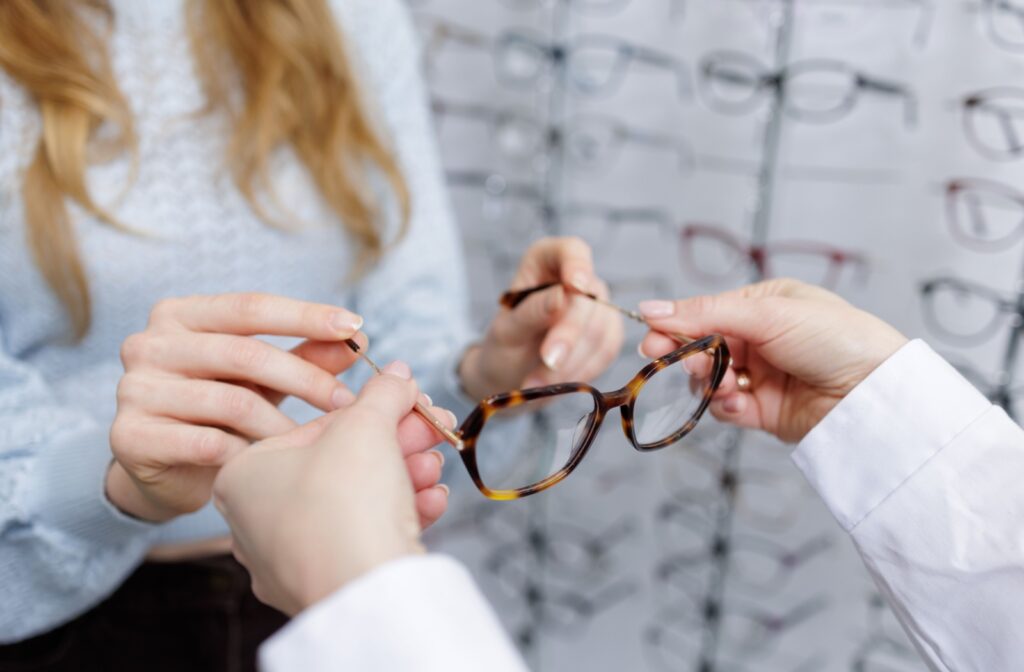 An optician handing a pair of glasses with anti-reflective coating to a patient to try them on.